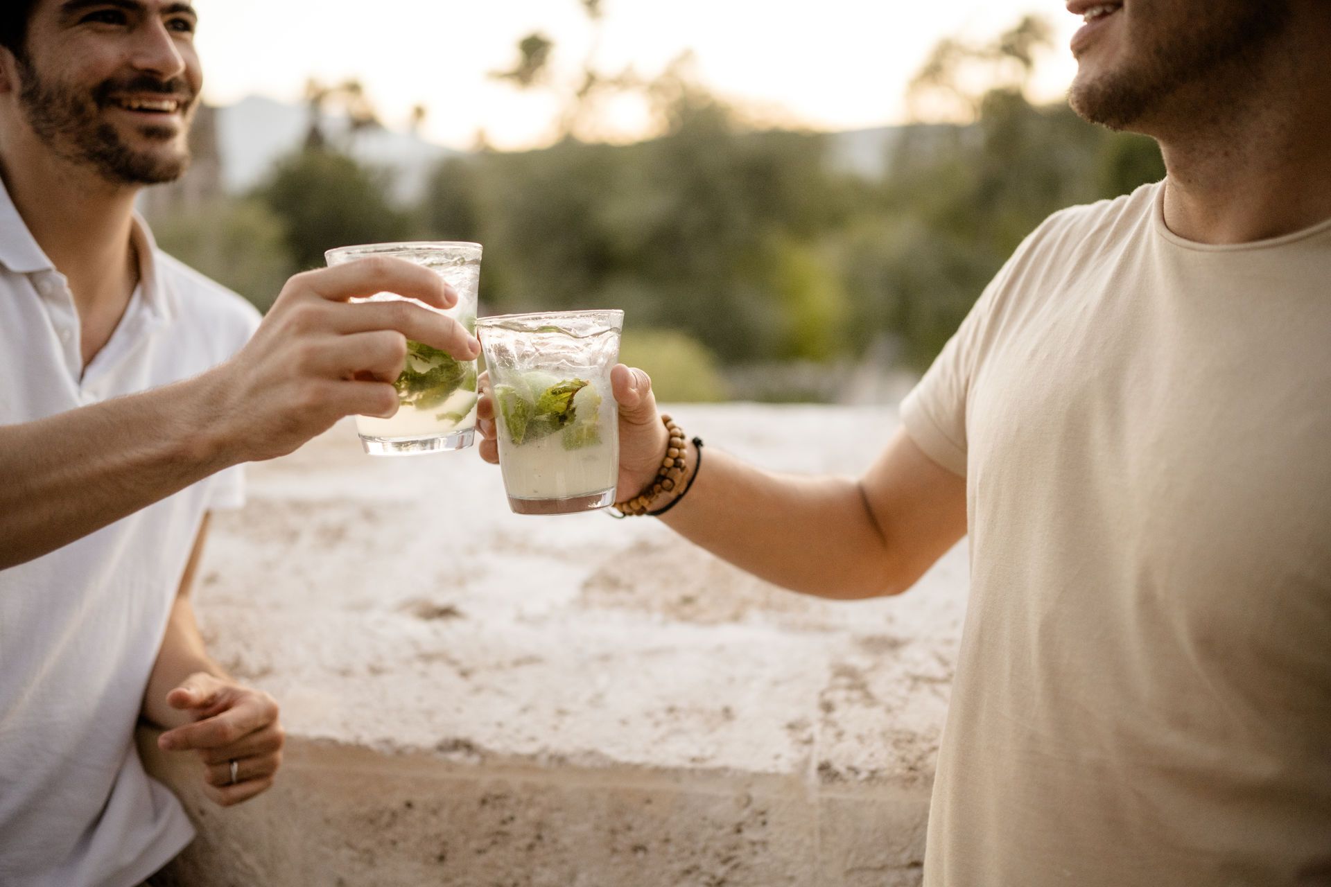 Dos personas chocan sus vasos de bebidas heladas al aire libre al atardecer.