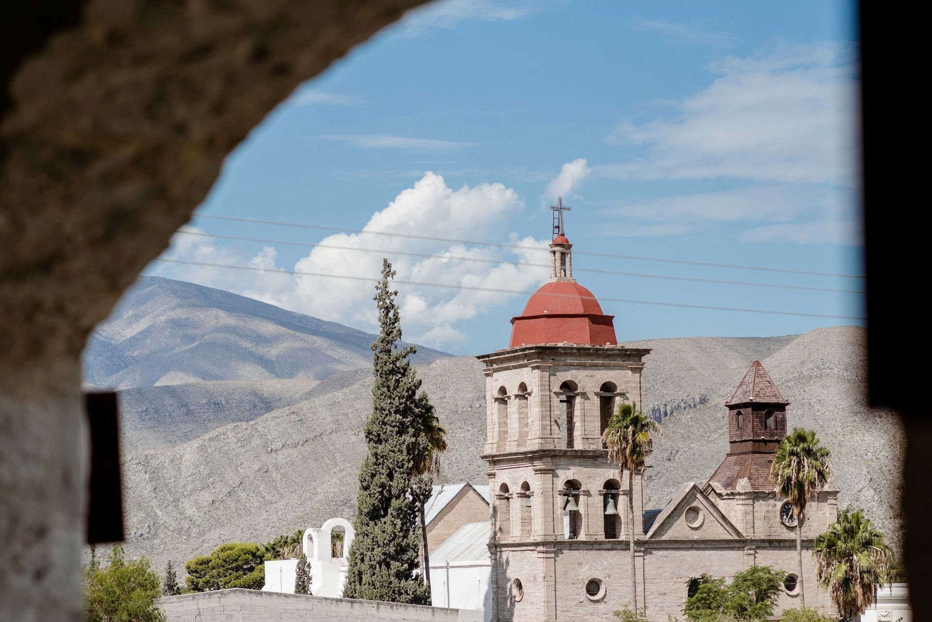 Iglesia de piedra con cúpula roja y campanario en un pueblo de montaña bajo un cielo azul.