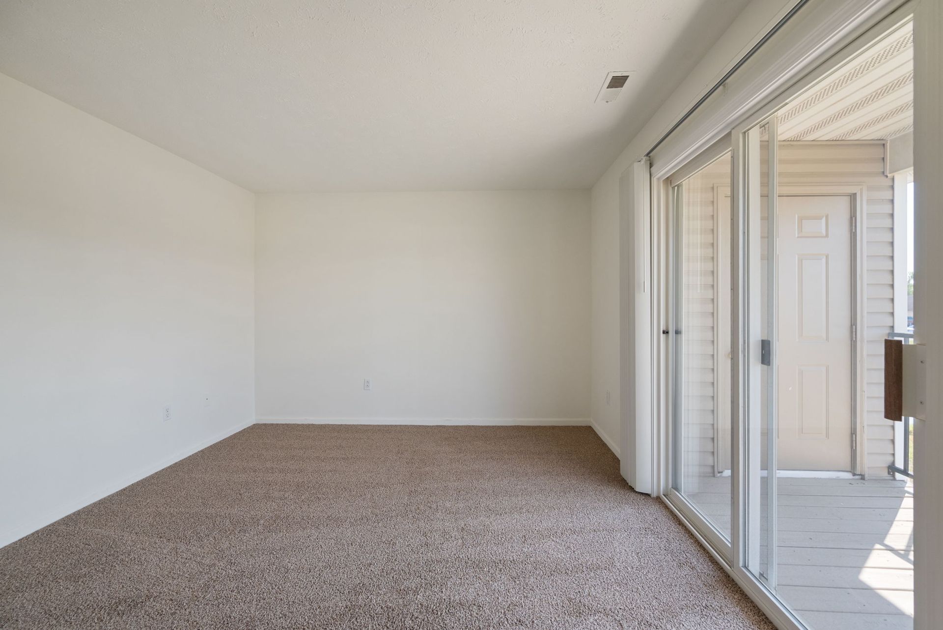 An empty living room with a sliding glass door and a balcony.