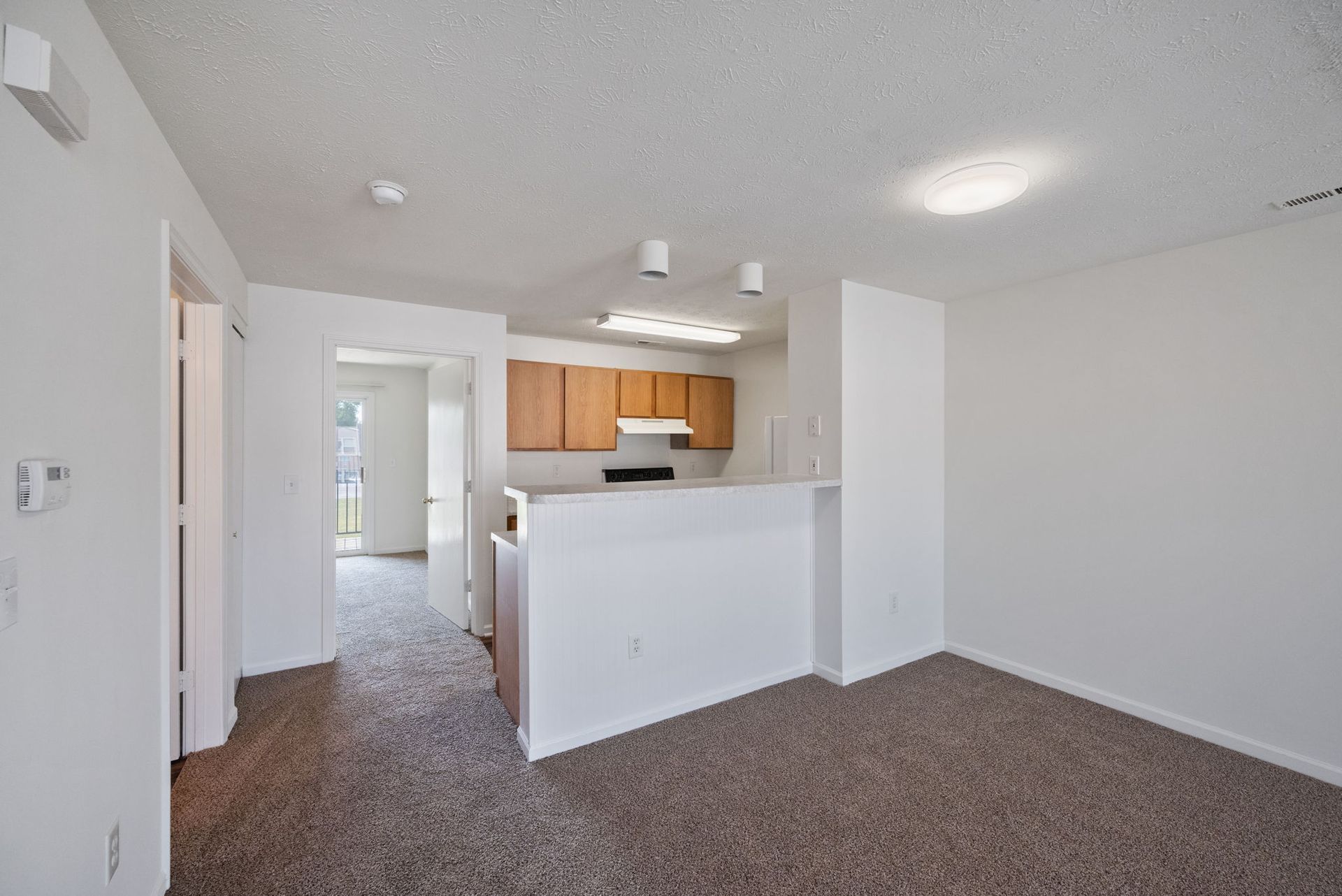 An empty living room with a kitchen in the background