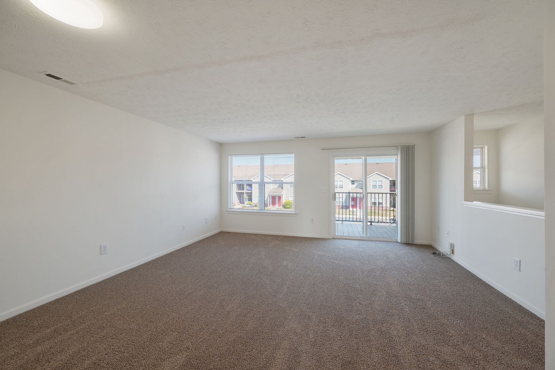 An empty living room with a sliding glass door and a balcony.