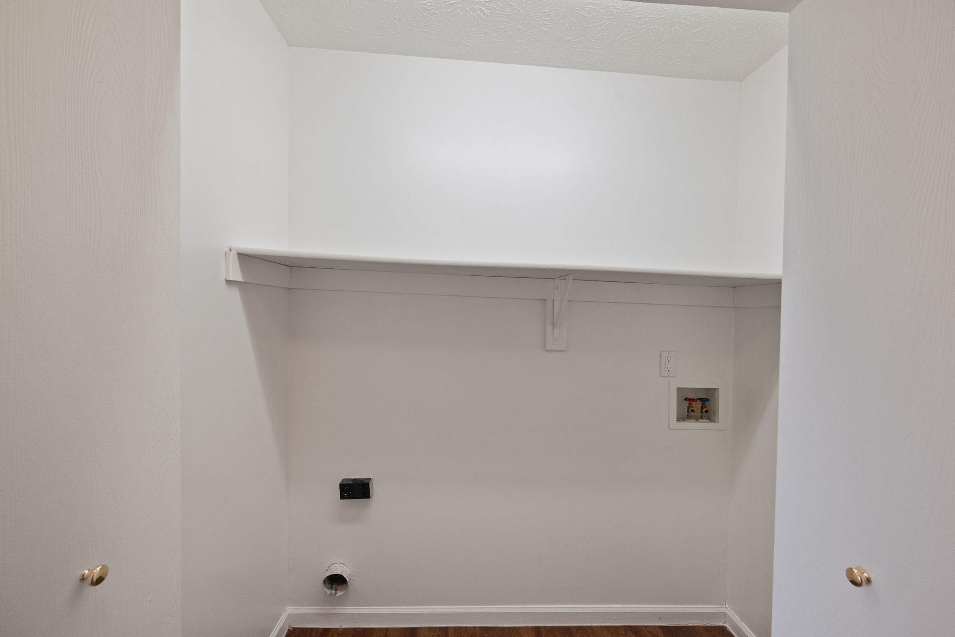 An empty laundry room with a shelf and a sink.