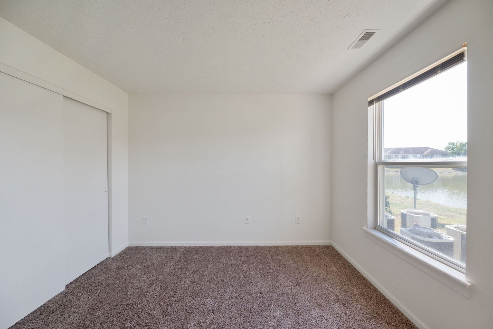 An empty bedroom with a window and a satellite dish