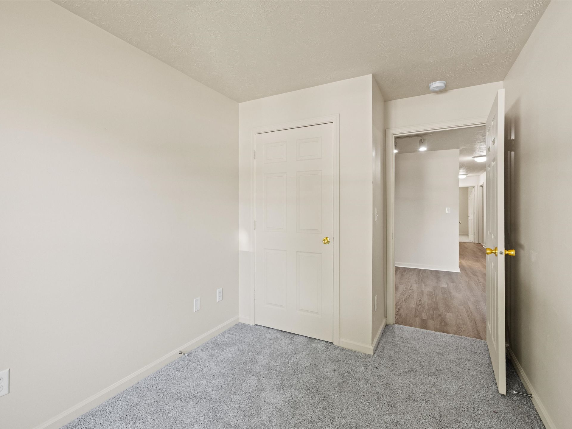 An empty bedroom with a closet and a door leading to a hallway.