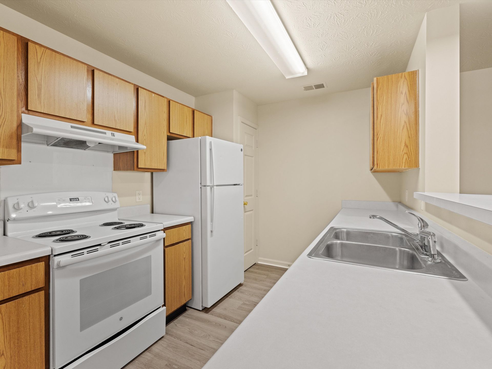 A kitchen with a stove , refrigerator , sink and wooden cabinets.