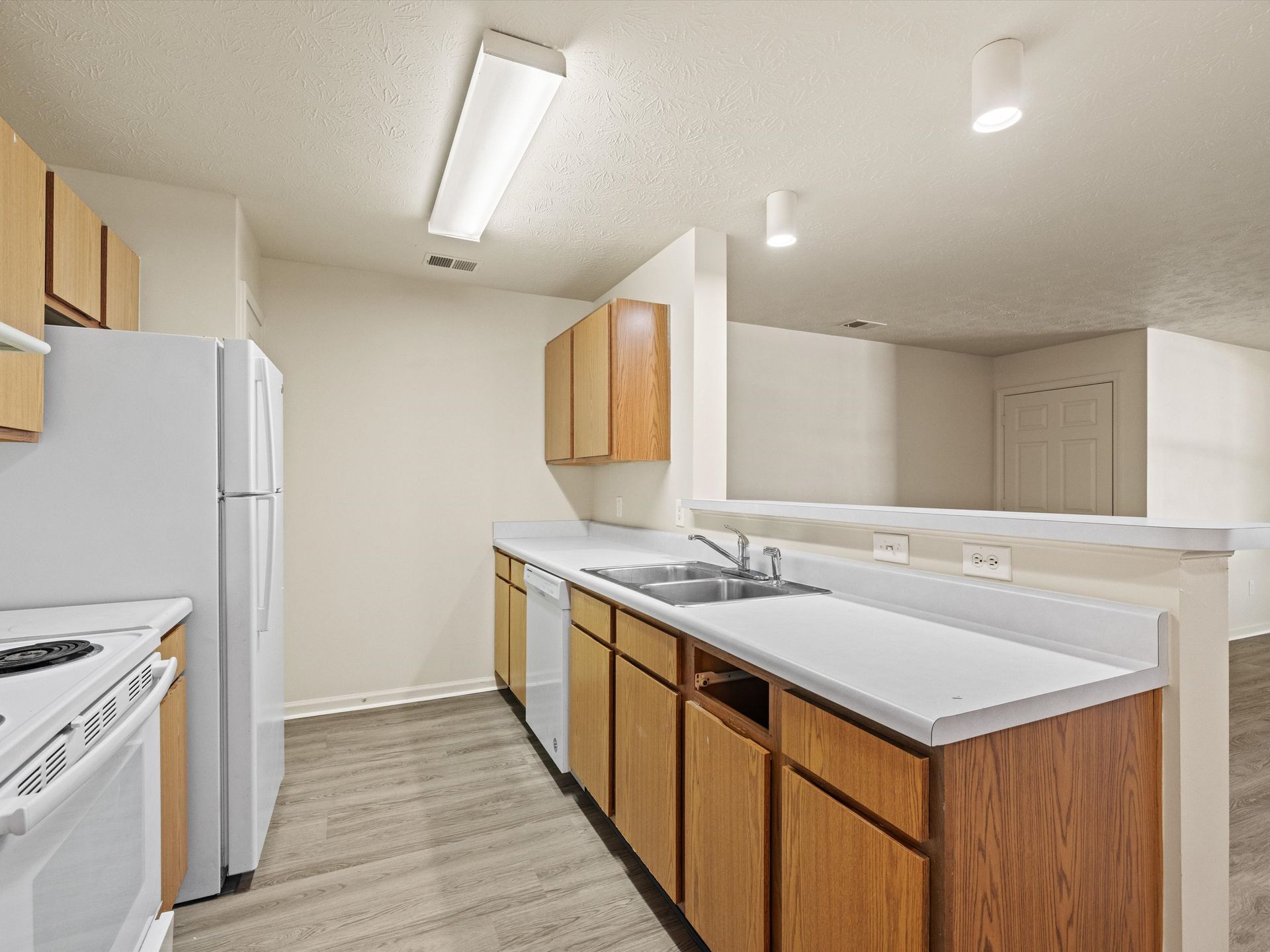 A kitchen with wooden cabinets , white appliances , a refrigerator and a sink.