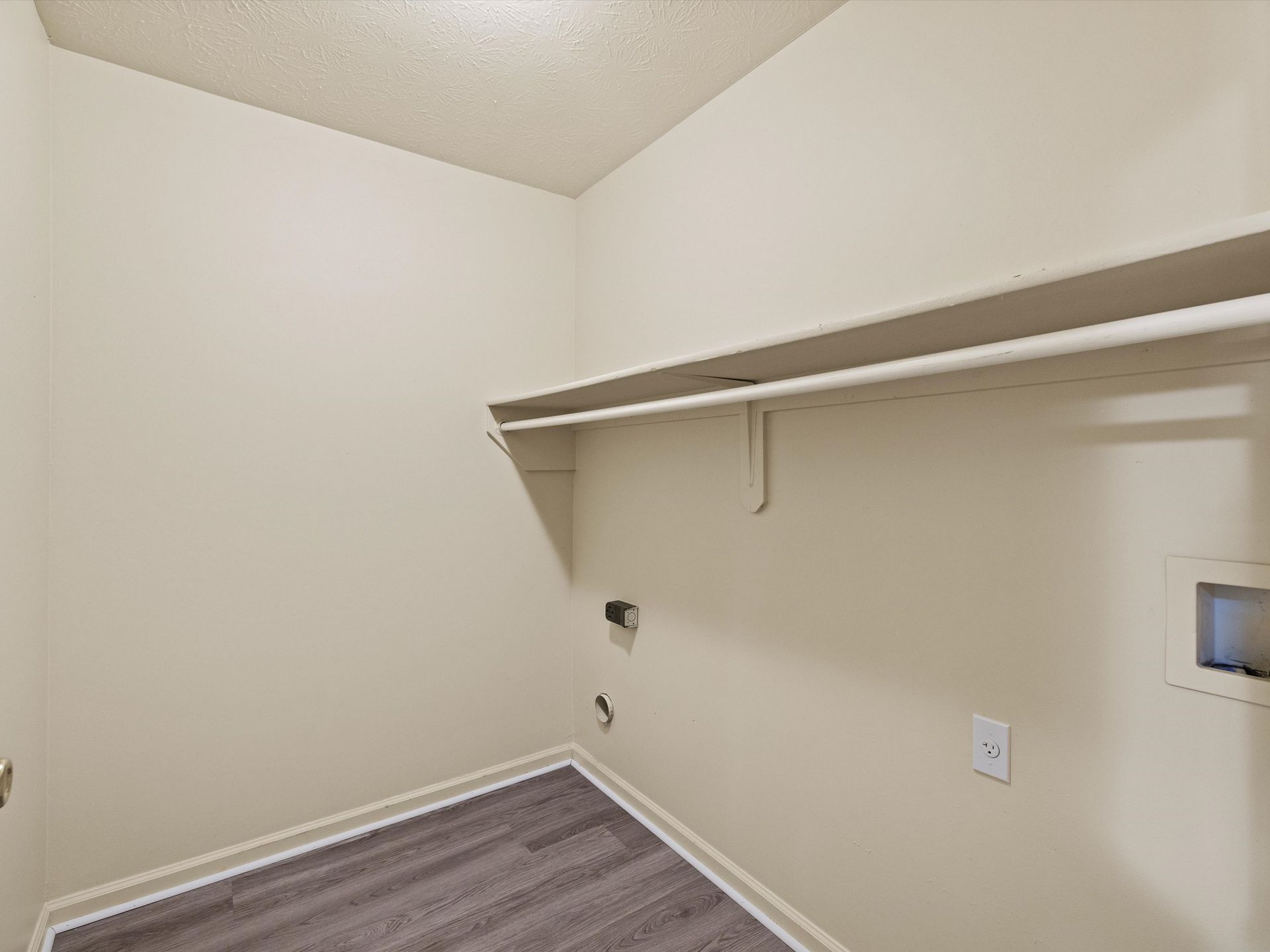 A laundry room with a wooden floor and a shelf.