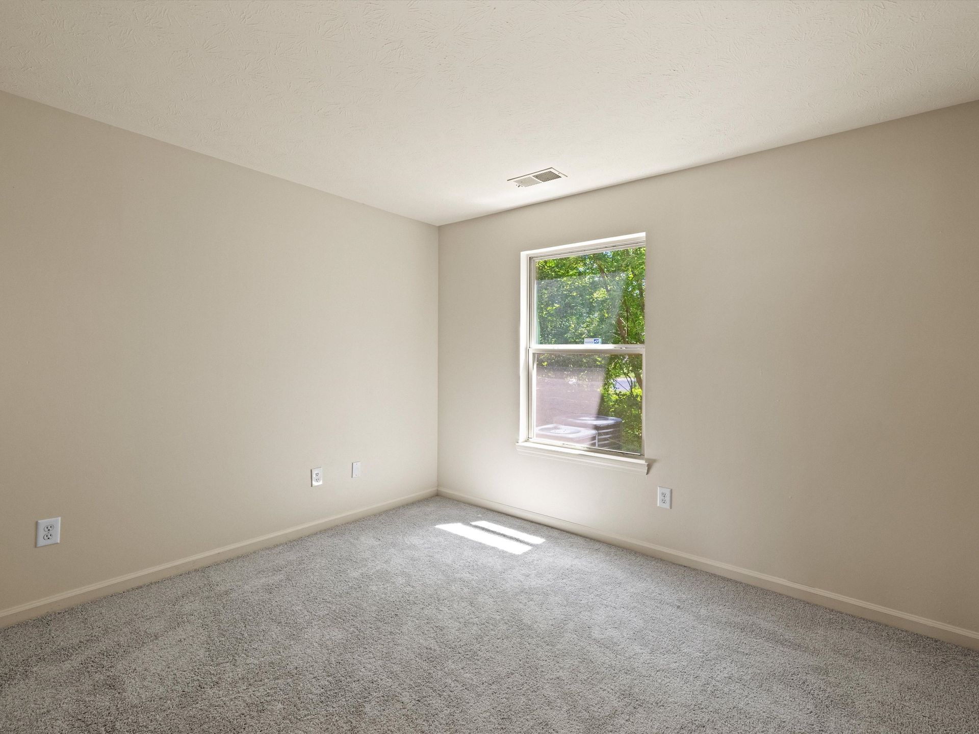 An empty bedroom with a window and a carpeted floor.