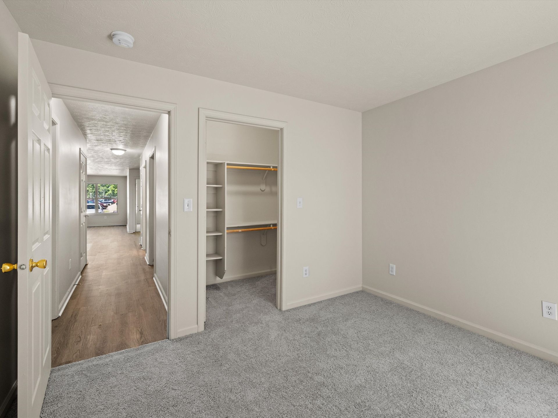 An empty bedroom with a walk in closet and a hallway leading to the living room.