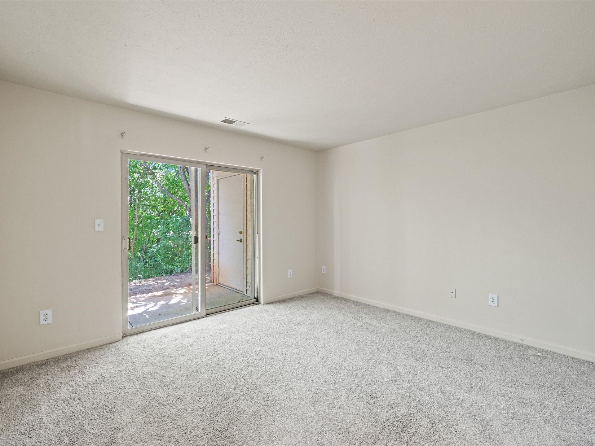 An empty living room with a sliding glass door leading to a patio.