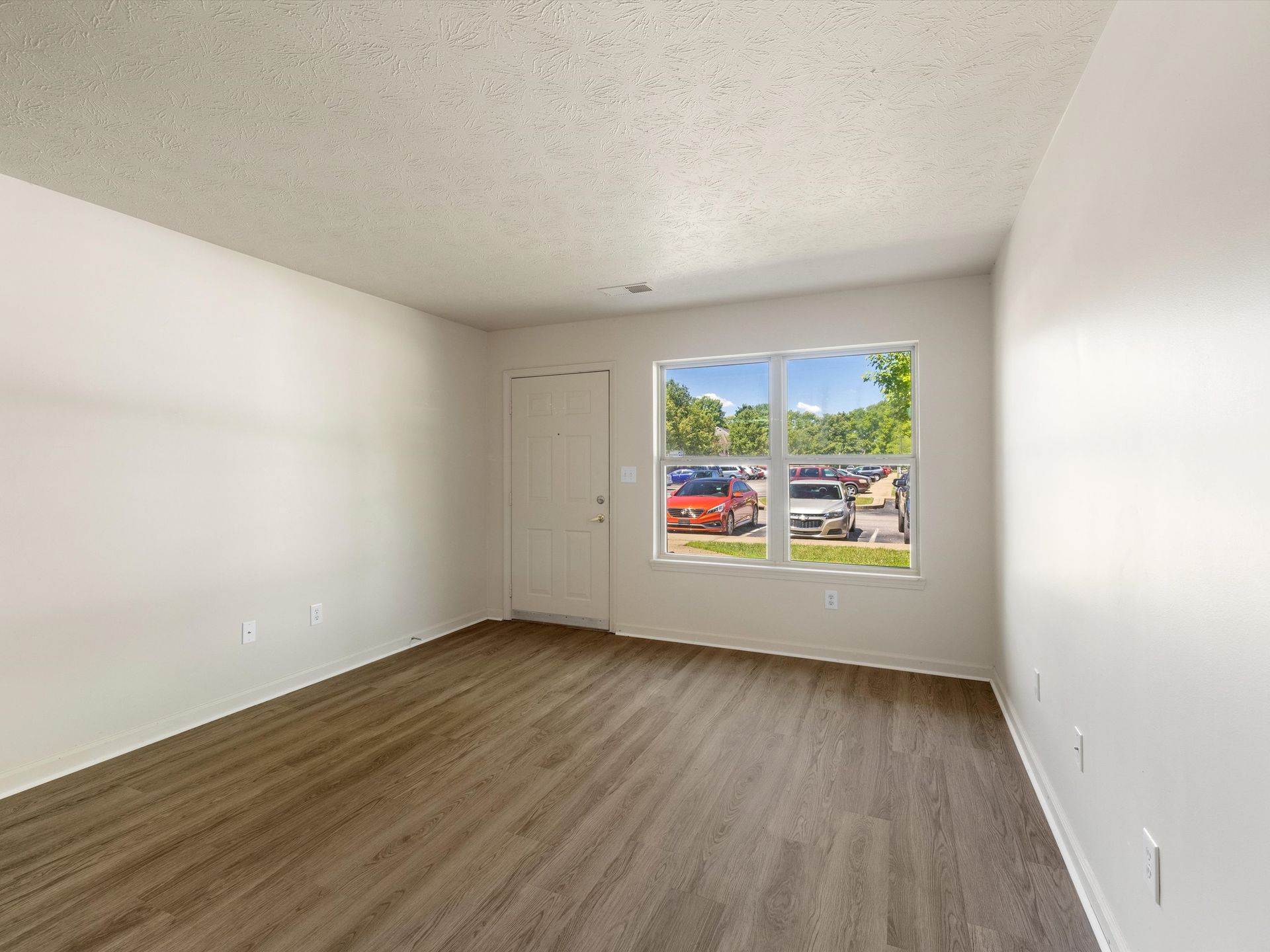 An empty living room with hardwood floors and two windows.