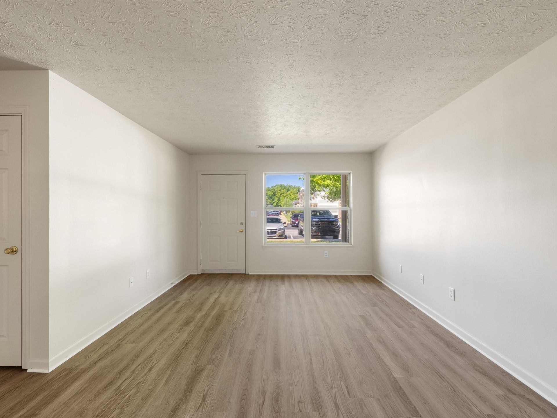 An empty living room with hardwood floors and white walls.