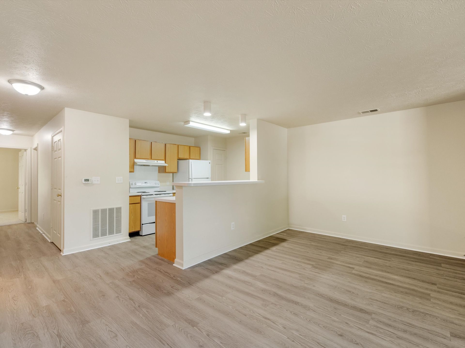 A living room with hardwood floors and a kitchen in the background.