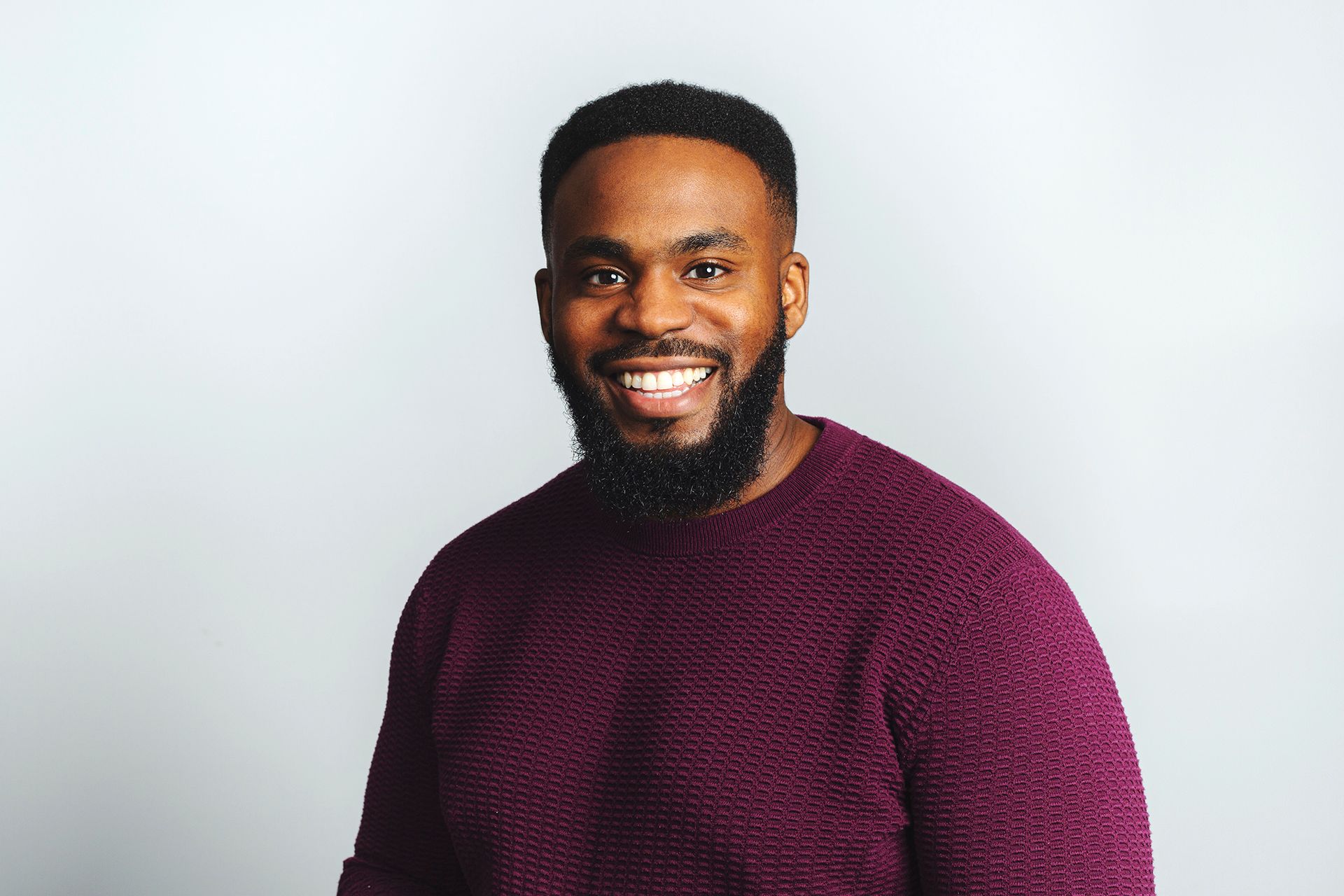 Smiling man in a burgundy sweater against a light gray background