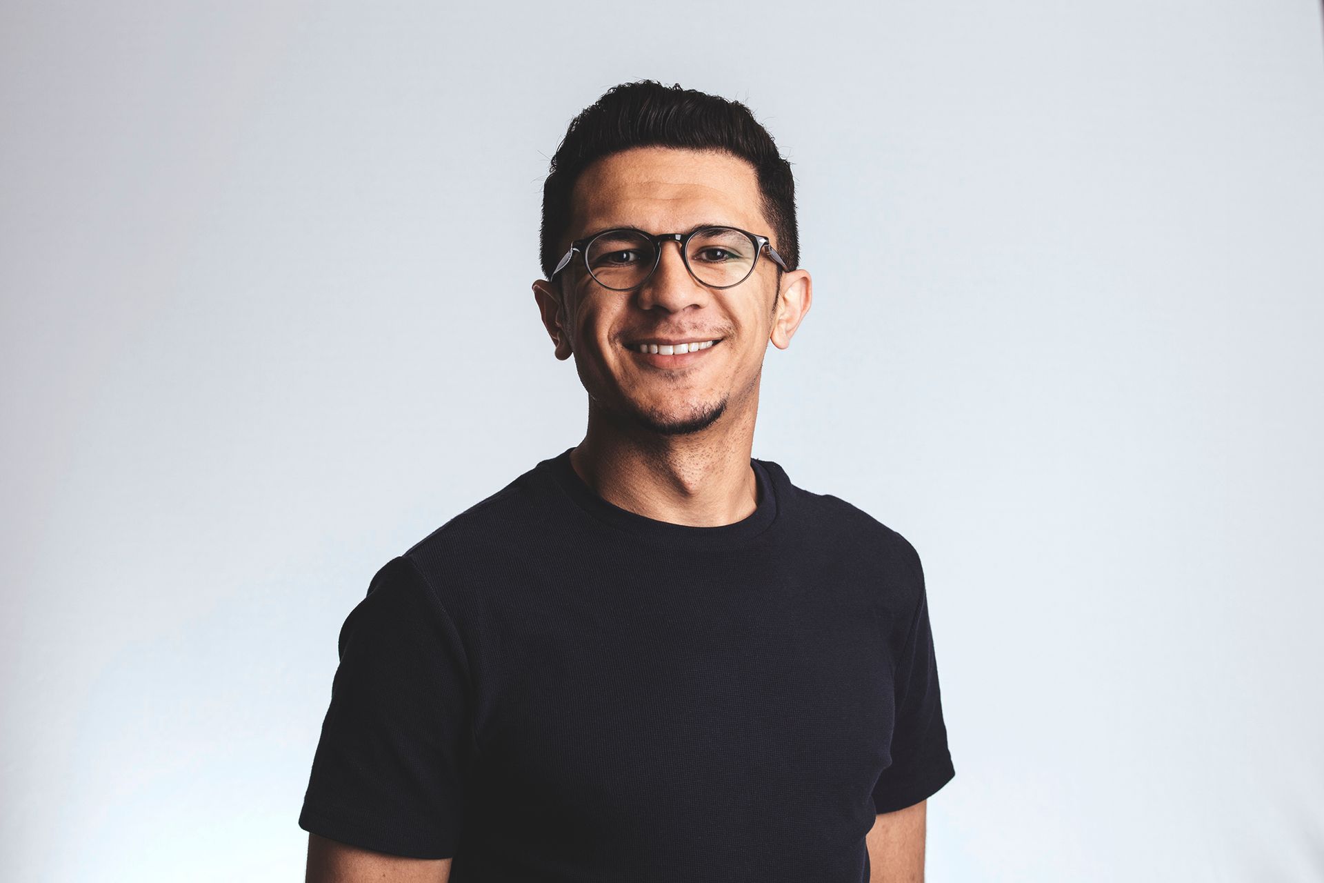 Smiling man in glasses and a black T-shirt against a light gray background