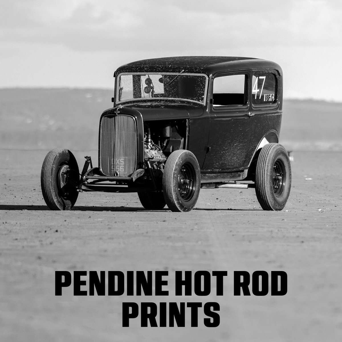 Black and white photo of a classic hot rod car on a sandy surface, 