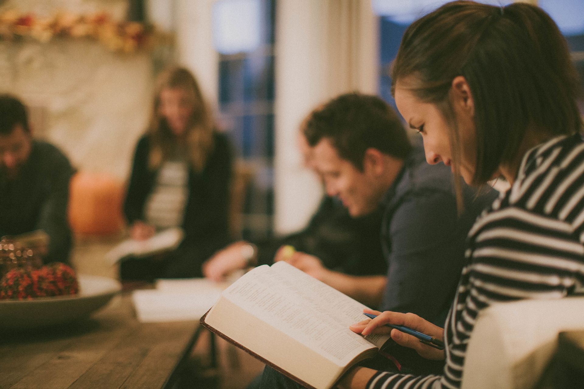 People reading books together in a cozy indoor gathering, with a woman in a striped shirt in the foreground