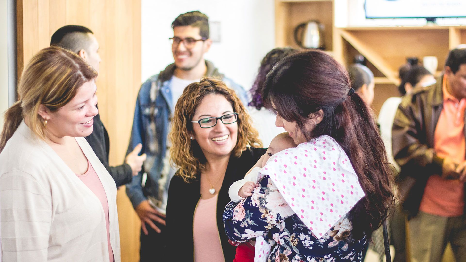 People chatting at a bright indoor gathering, smiling in a casual social setting.