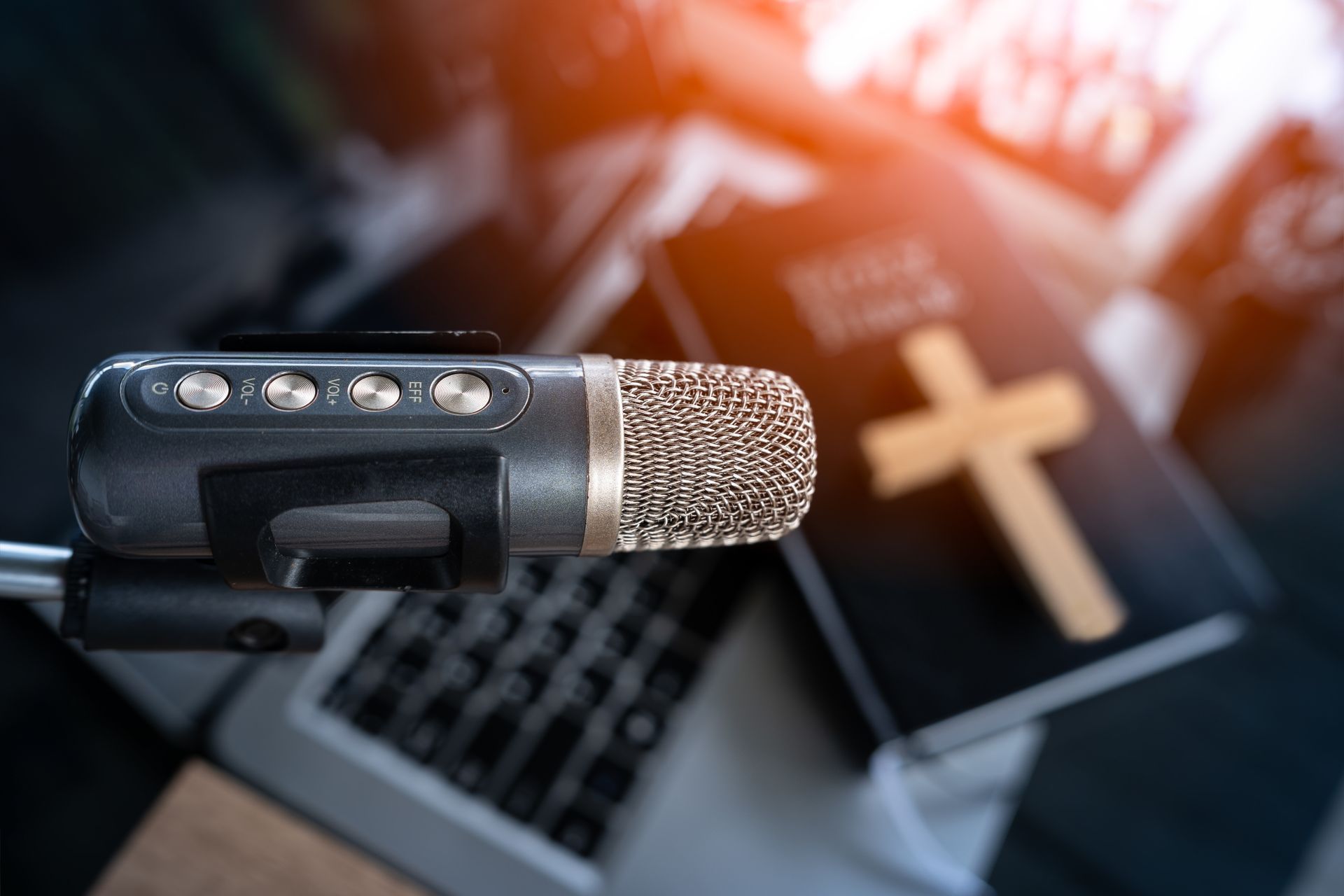 Microphone in foreground with laptop and glowing cross in the background, suggesting a church or worship setting