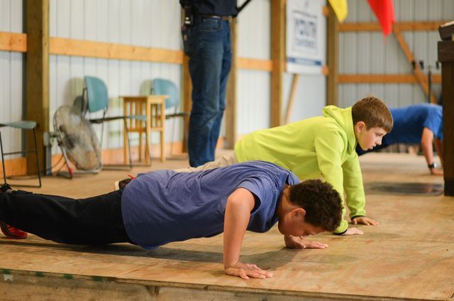 People doing push-ups in a gym, including one in a neon green shirt and one in a blue shirt.