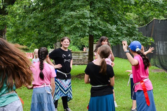 Group of people outdoors in a park, standing in a circle and raising their hands during an activity