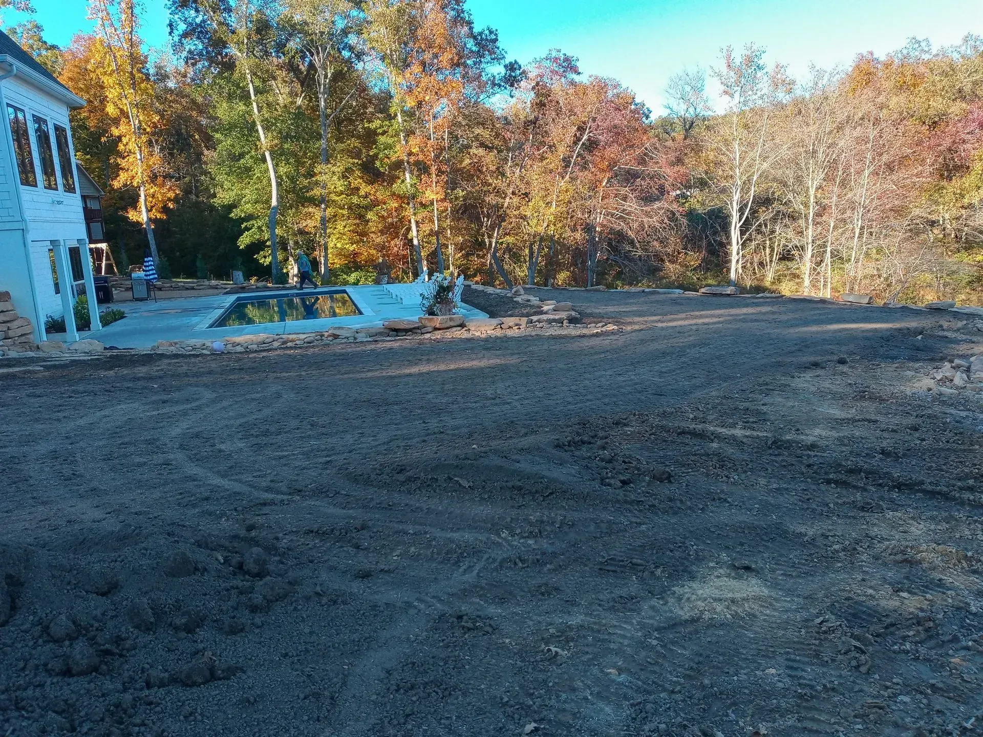 Freshly leveled dirt yard beside a white house, with autumn trees in the background