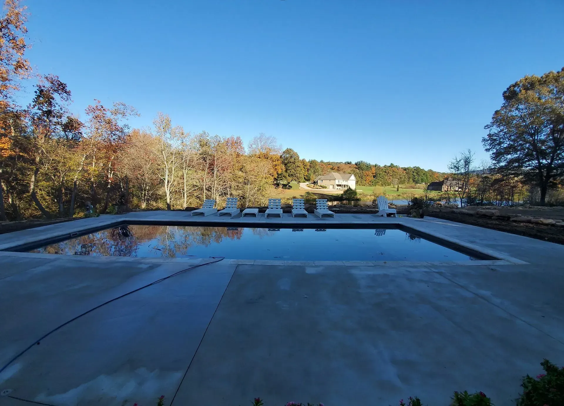 Reflecting pool in a park, bordered by autumn trees under a clear blue sky