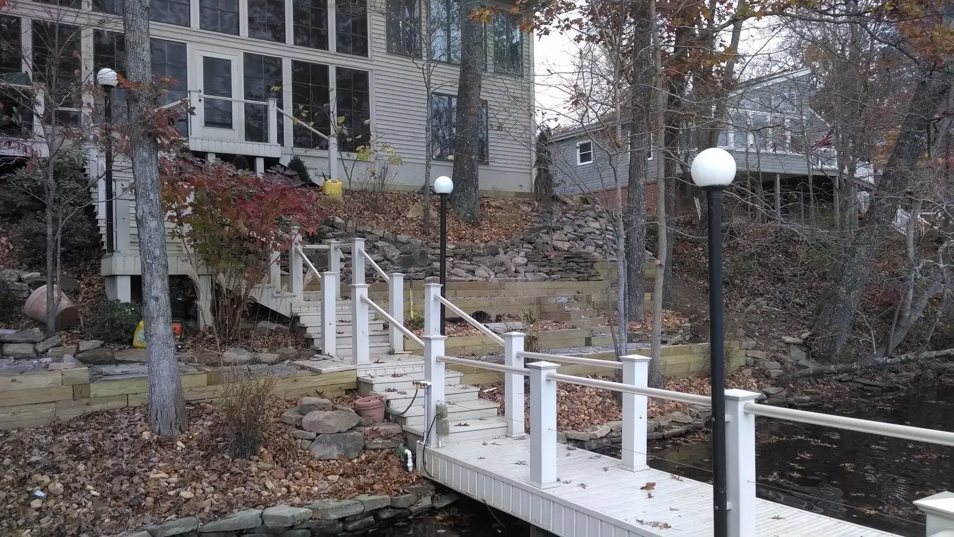 White wooden walkway with railings and globe lights leading up a wooded hillside to a house