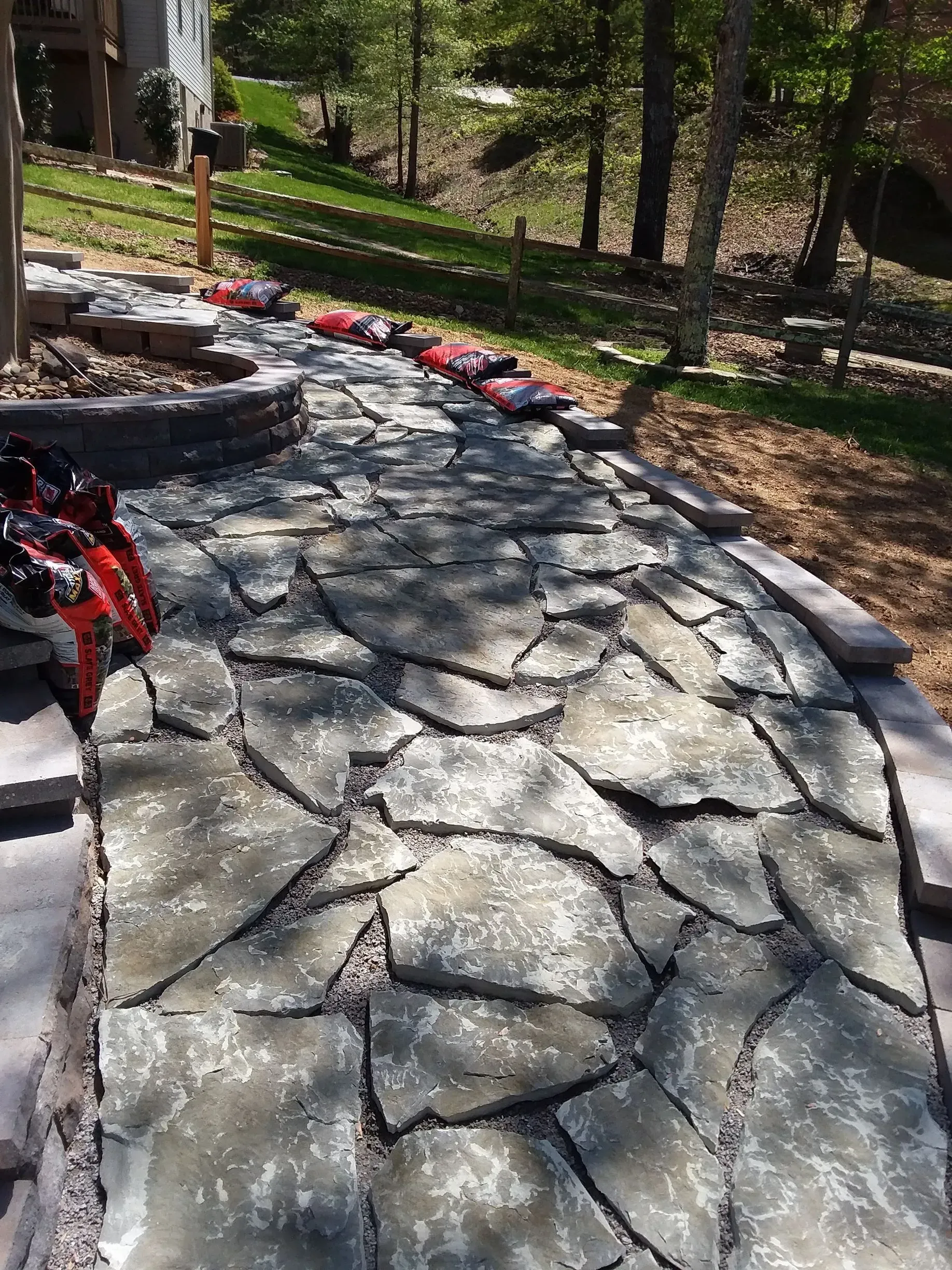 Stone walkway in a wooded yard with red leaves scattered along the edge.