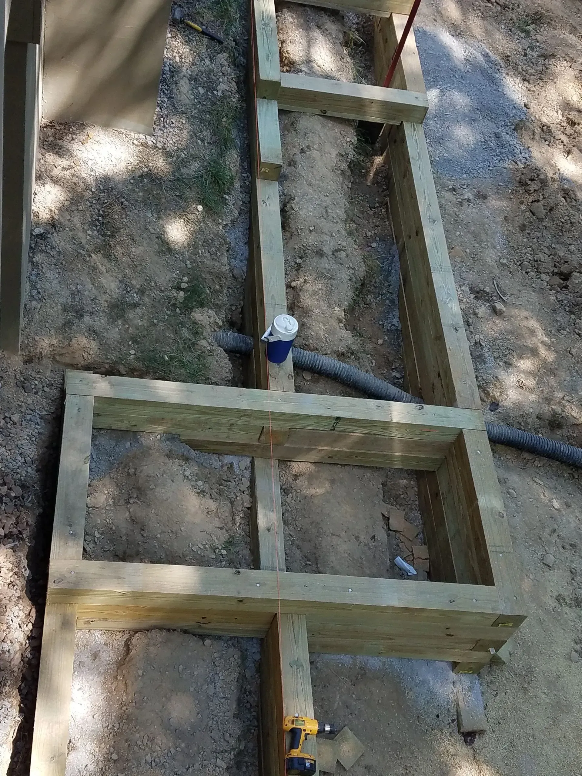 Wooden ladder frame laid on gravel, with a blue clamp near the center and a yellow clamp at the bottom.