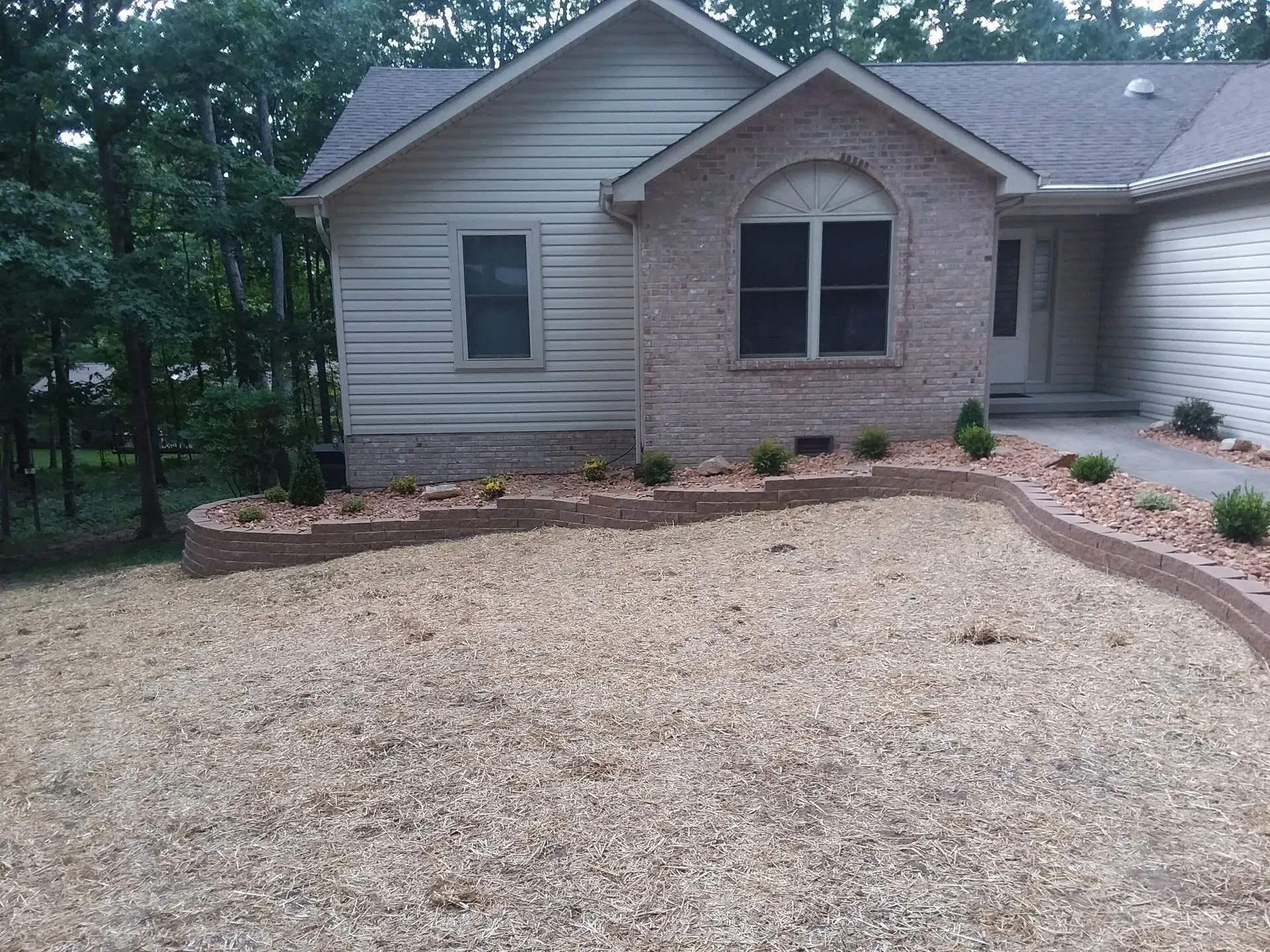 Front yard with tan gravel landscaping, stone edging, and a beige brick house with arched window.