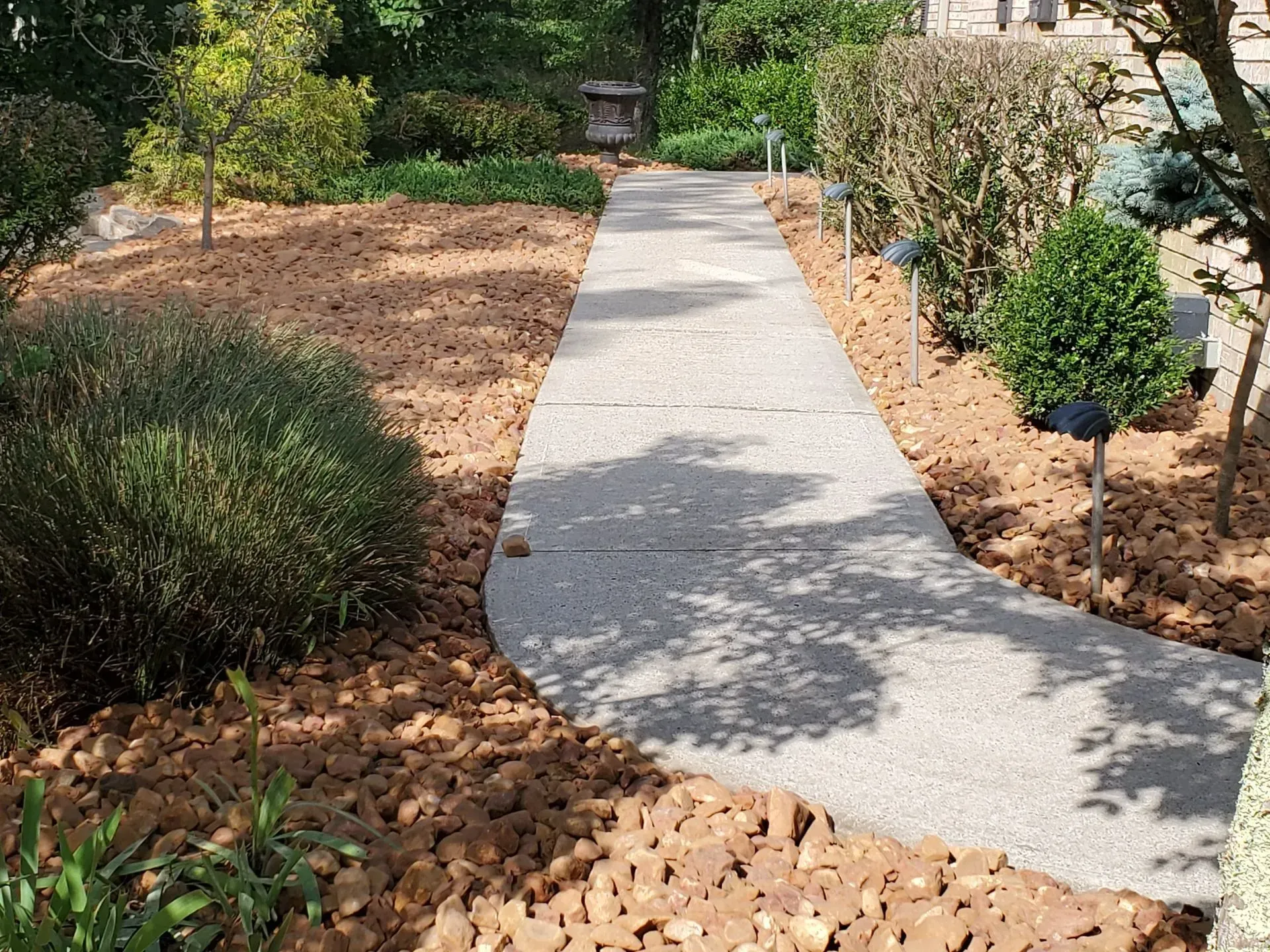 Curved concrete garden path bordered by mulch, shrubs, and trees in a landscaped yard