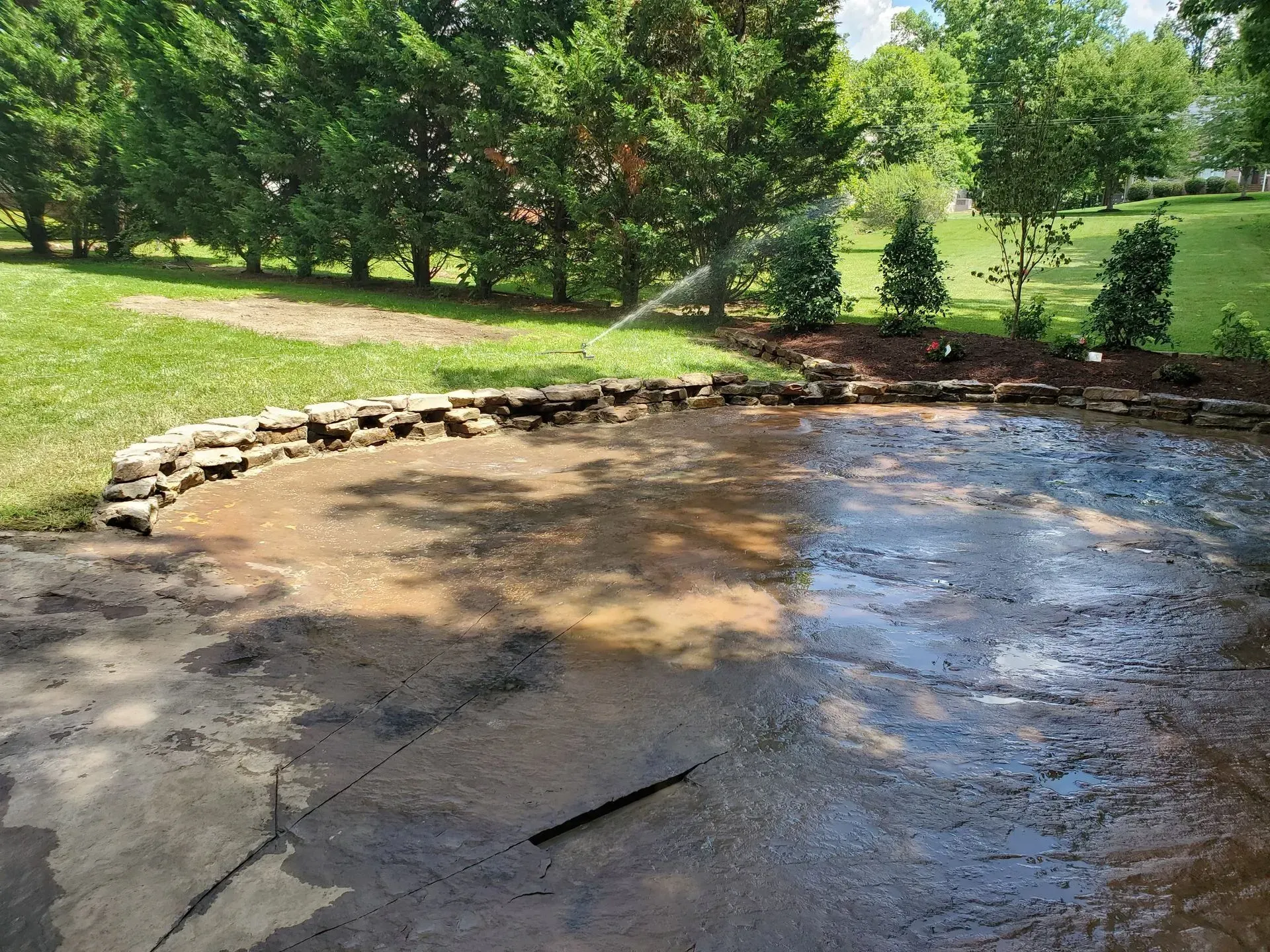 Shallow water over a curved concrete surface beside a grassy park and trees