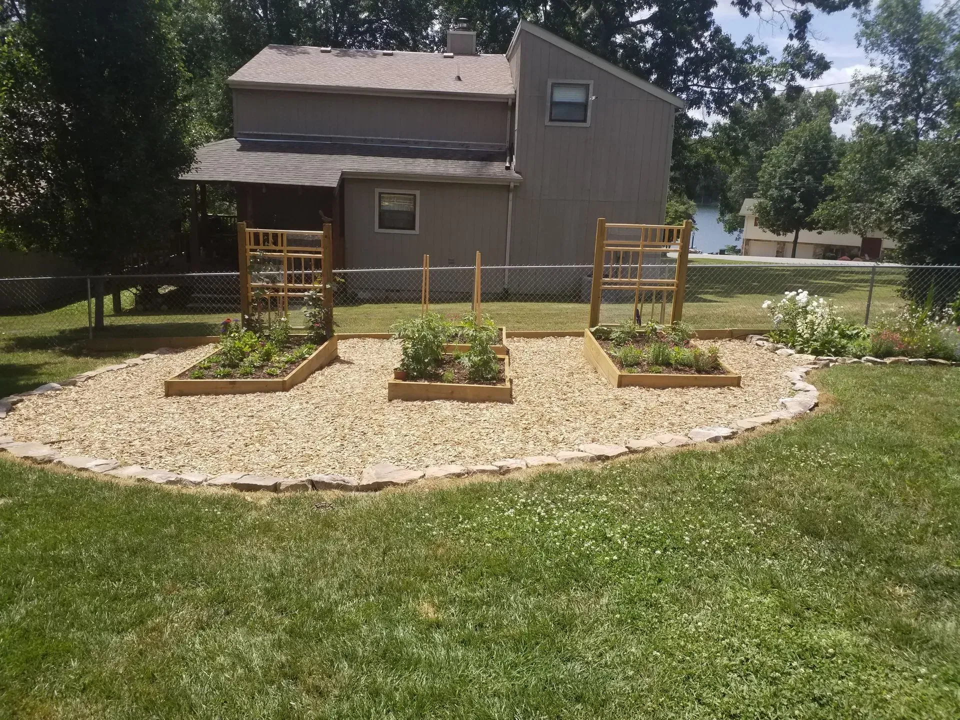 Backyard garden with raised beds and mulch path in front of a gray house
