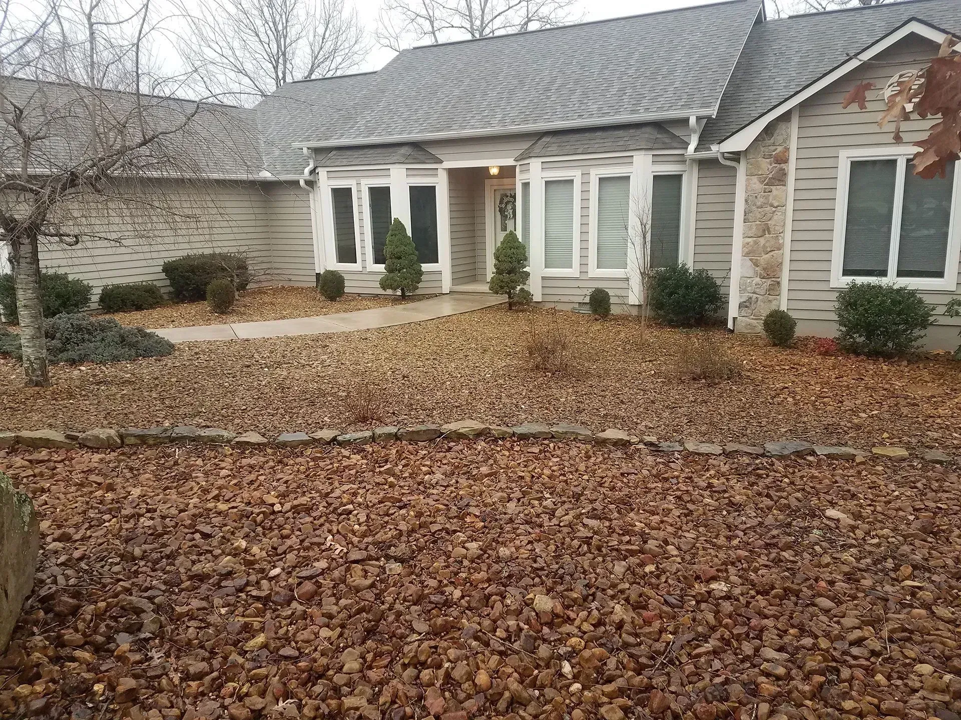Suburban house with a leaf-covered front yard, bare trees, and a small stone patio.
