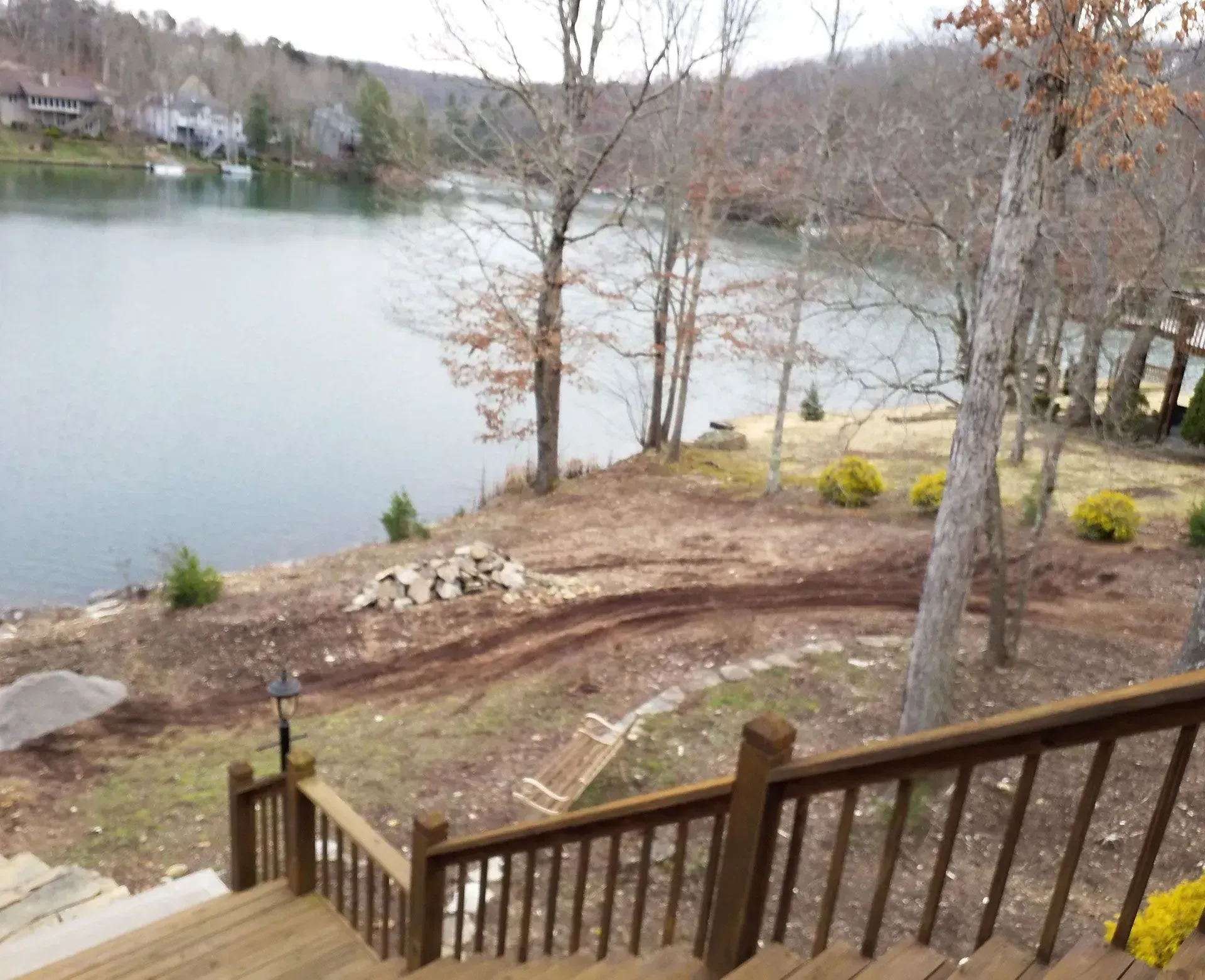 Deck overlooking a calm lake with bare trees and a dirt path along the shore