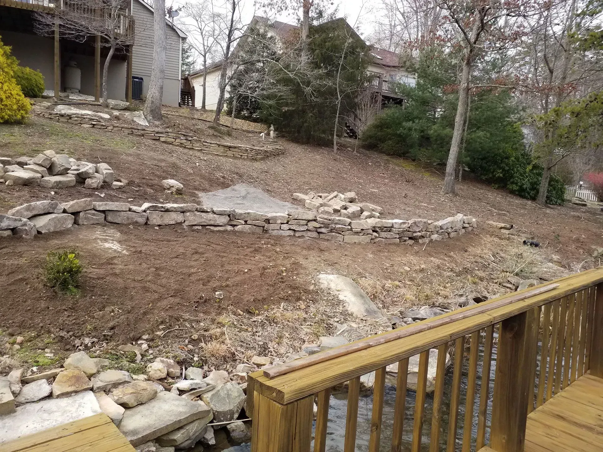 Wooden deck overlooking a rocky, leaf-strewn backyard with trees and a house in the background
