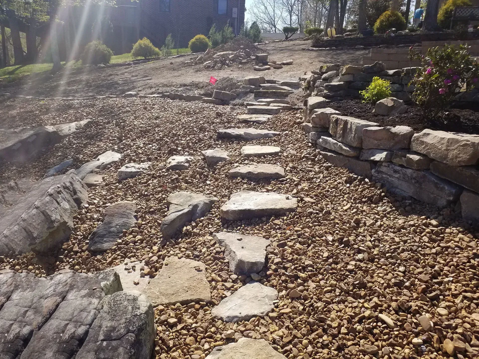 Stone steps leading up a rocky garden path with sunlight and bare trees above