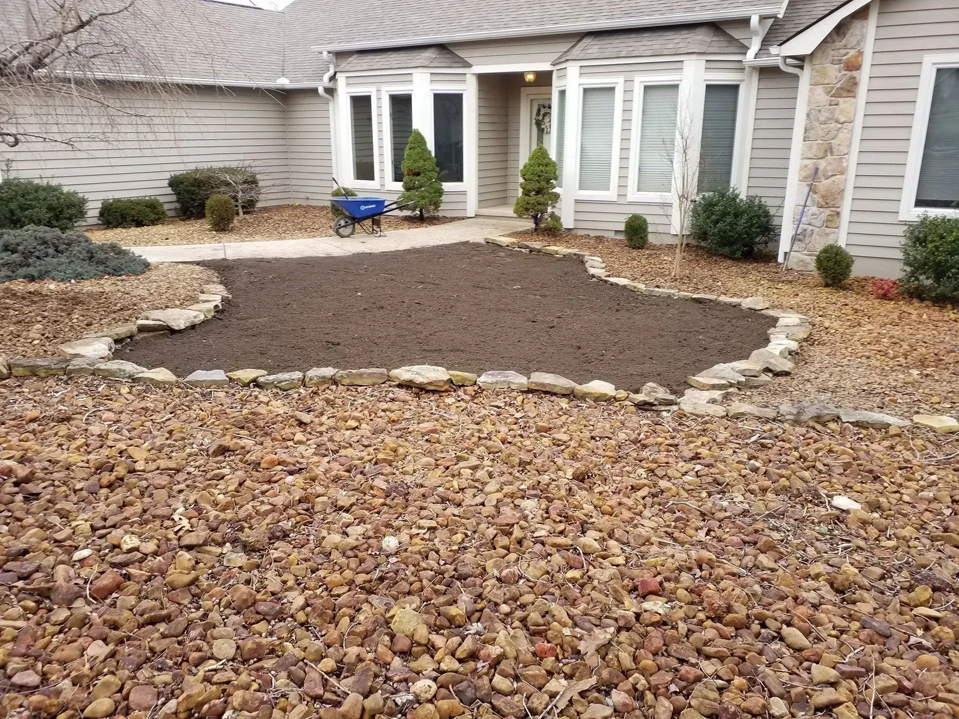 Front yard landscaping with a mulched bed, stone border, and a blue chair near the house.
