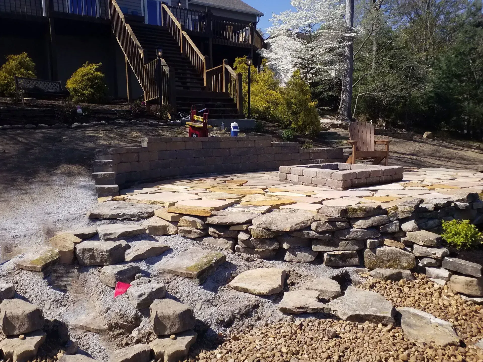 Stone patio and fire pit in a backyard with a house and trees in the background