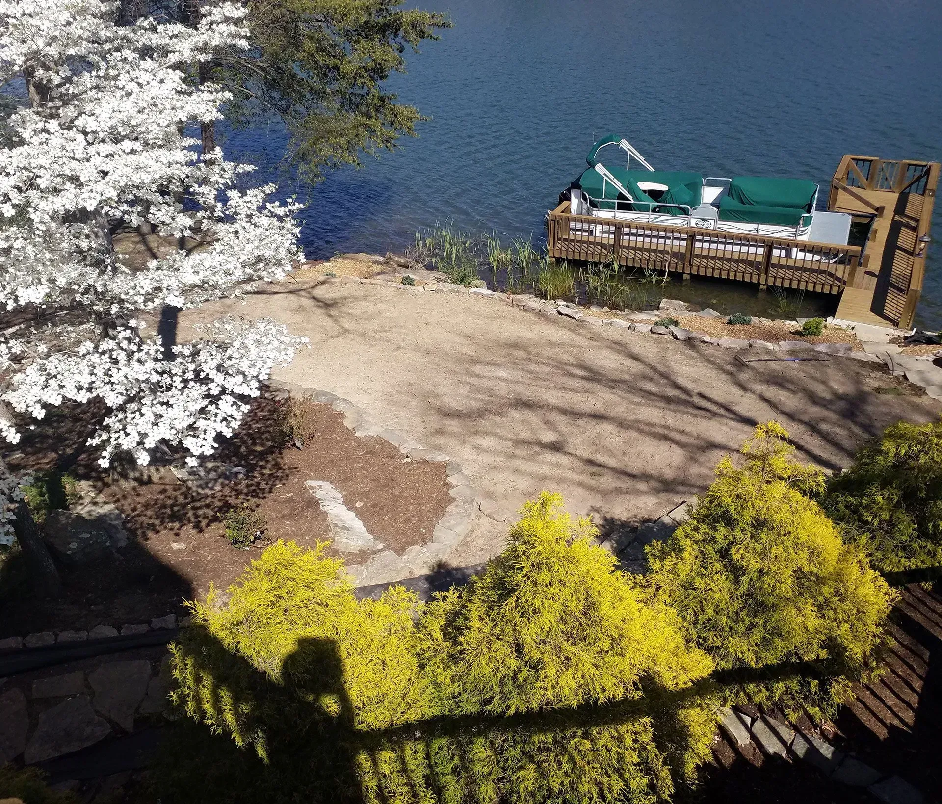 Lakeside dock with green kayaks, blue water, and blooming trees beside a sandy shore