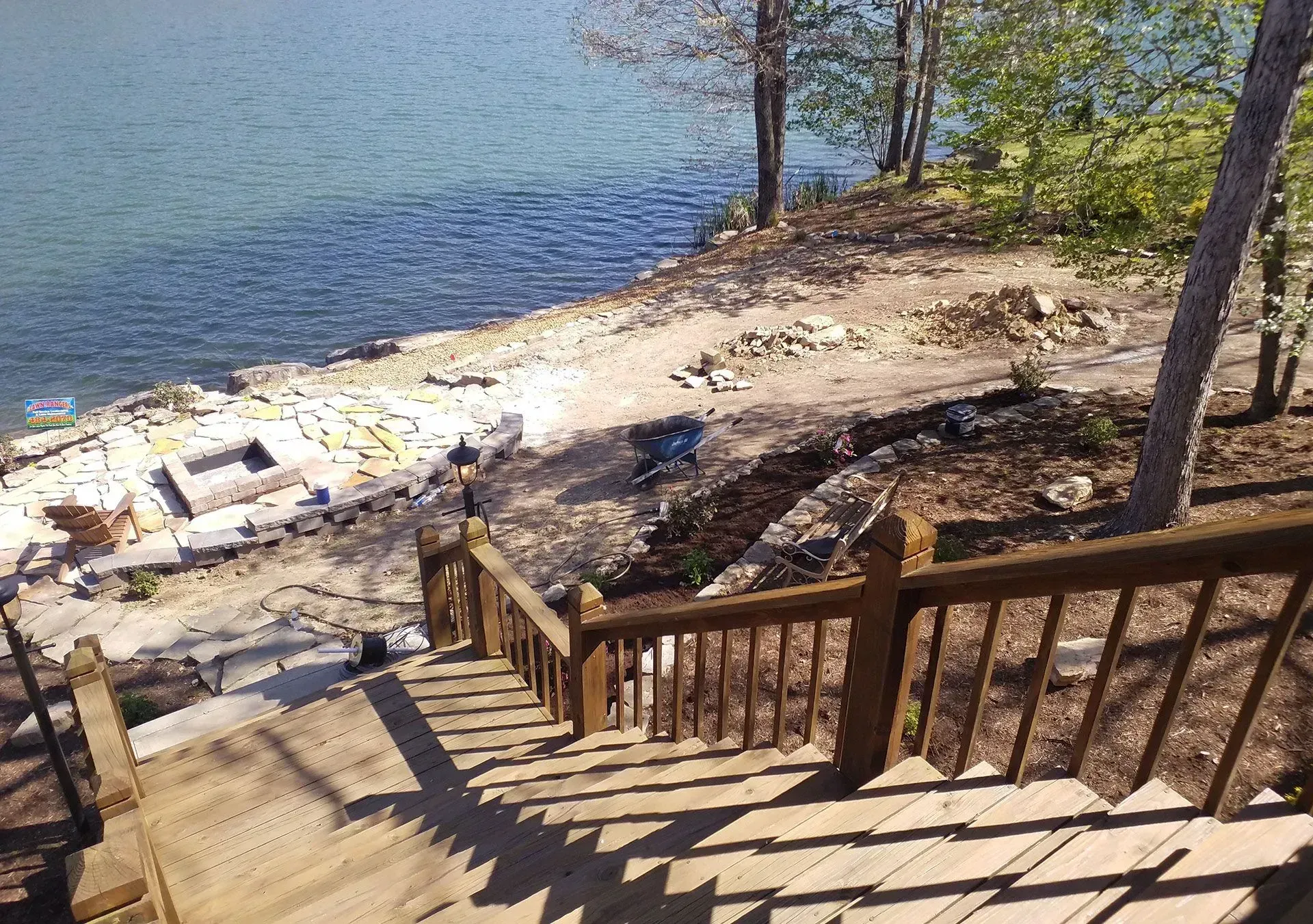 Wooden stairs leading to a rocky lakeshore with calm blue water and trees on the bank