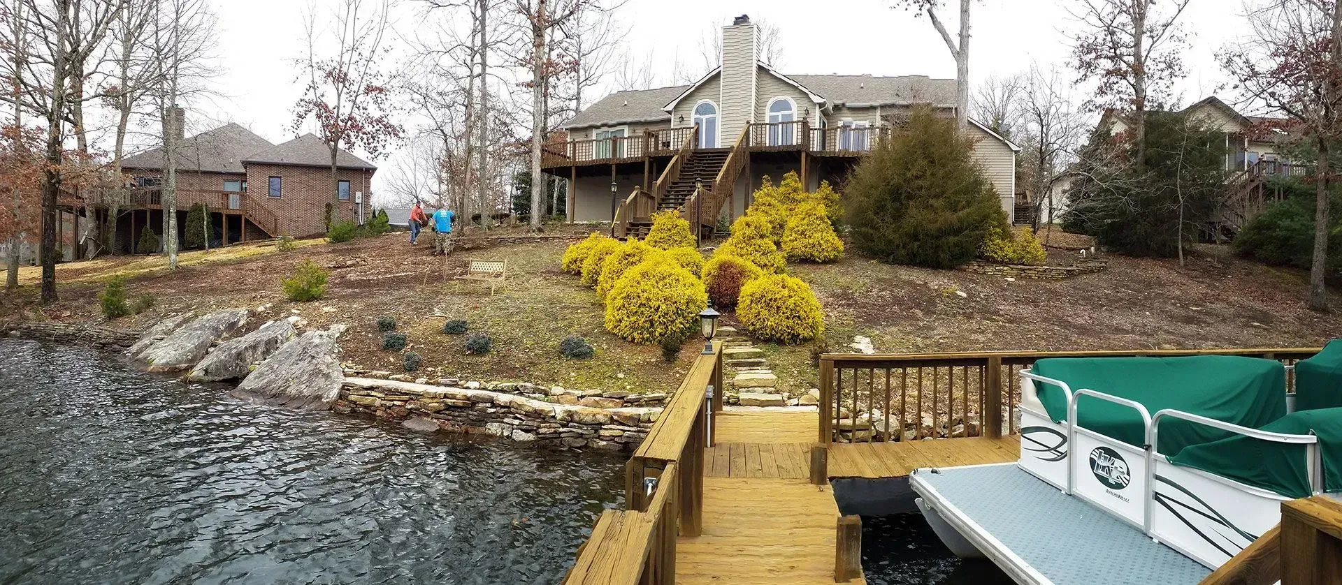 Lakeside house with wooden dock, rocky shoreline, and a small boat in the foreground