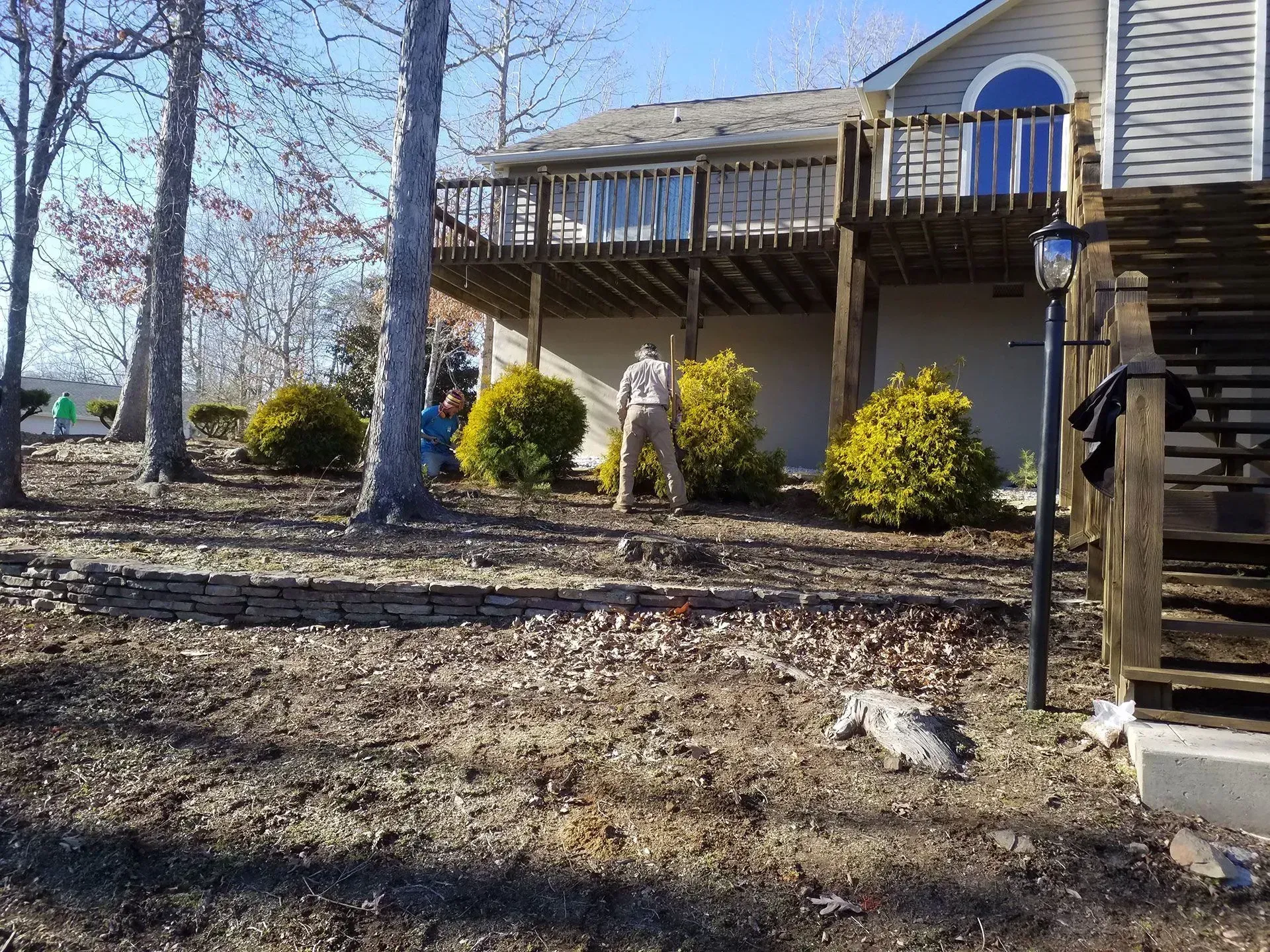 Back deck with stairs, bare trees, and a rocky yard beside a beige house.