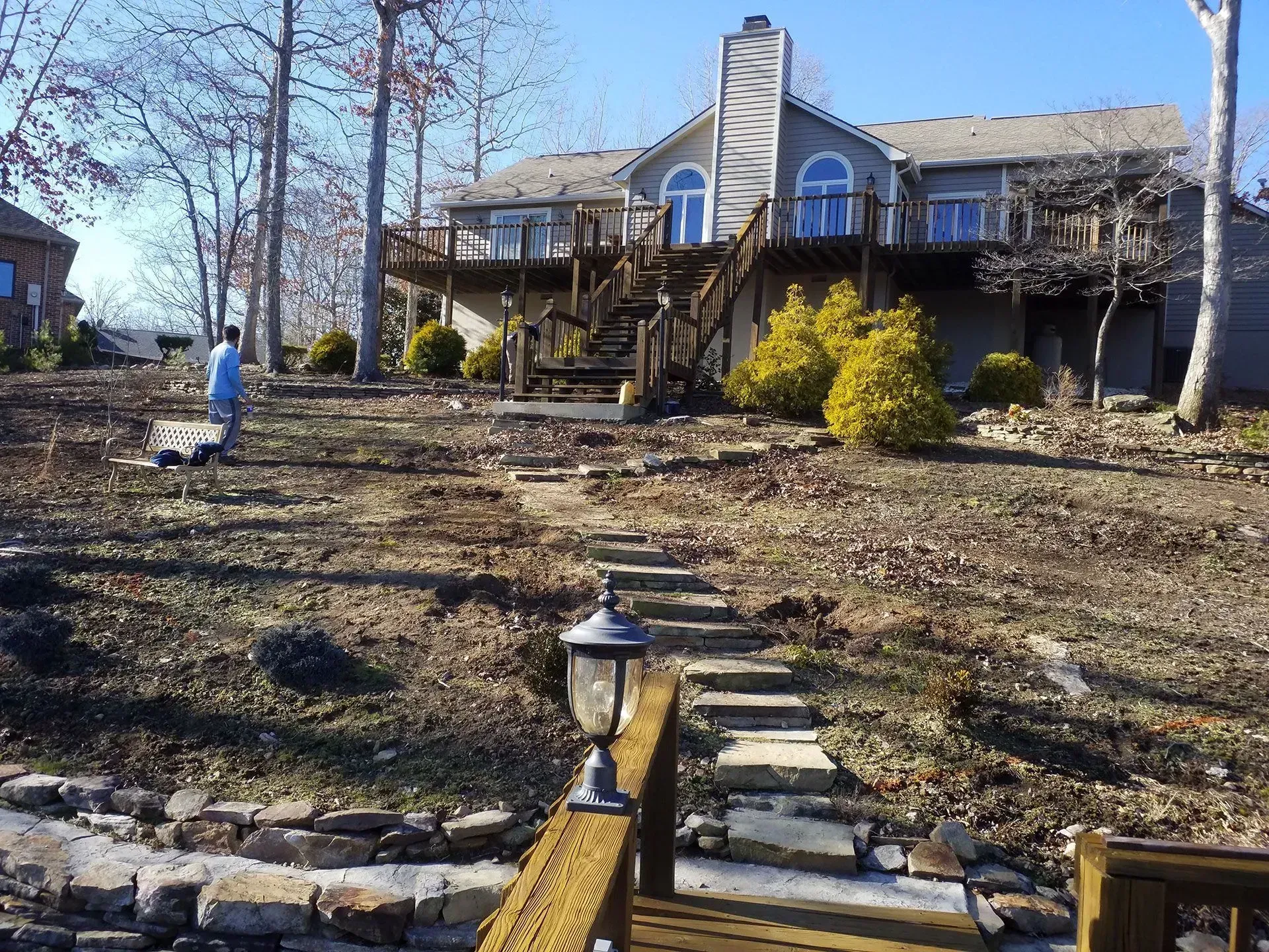 House with stone walkway and lamp posts in a leaf-covered yard on a sunny day
