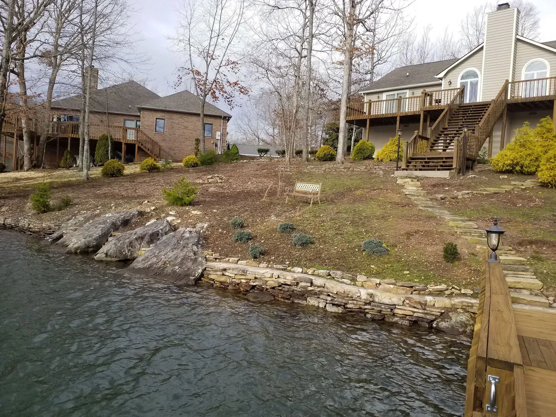 Lakefront homes beside rocky shoreline and calm water on a gray day