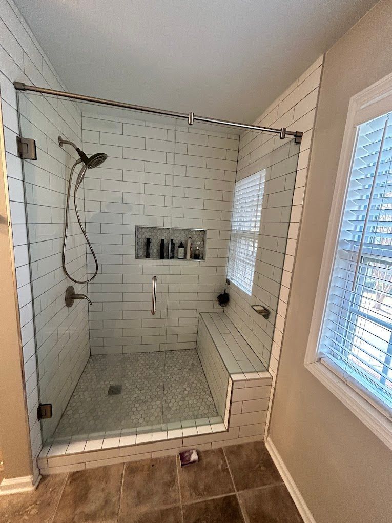 A bathroom with a walk in shower with a glass door and a window.