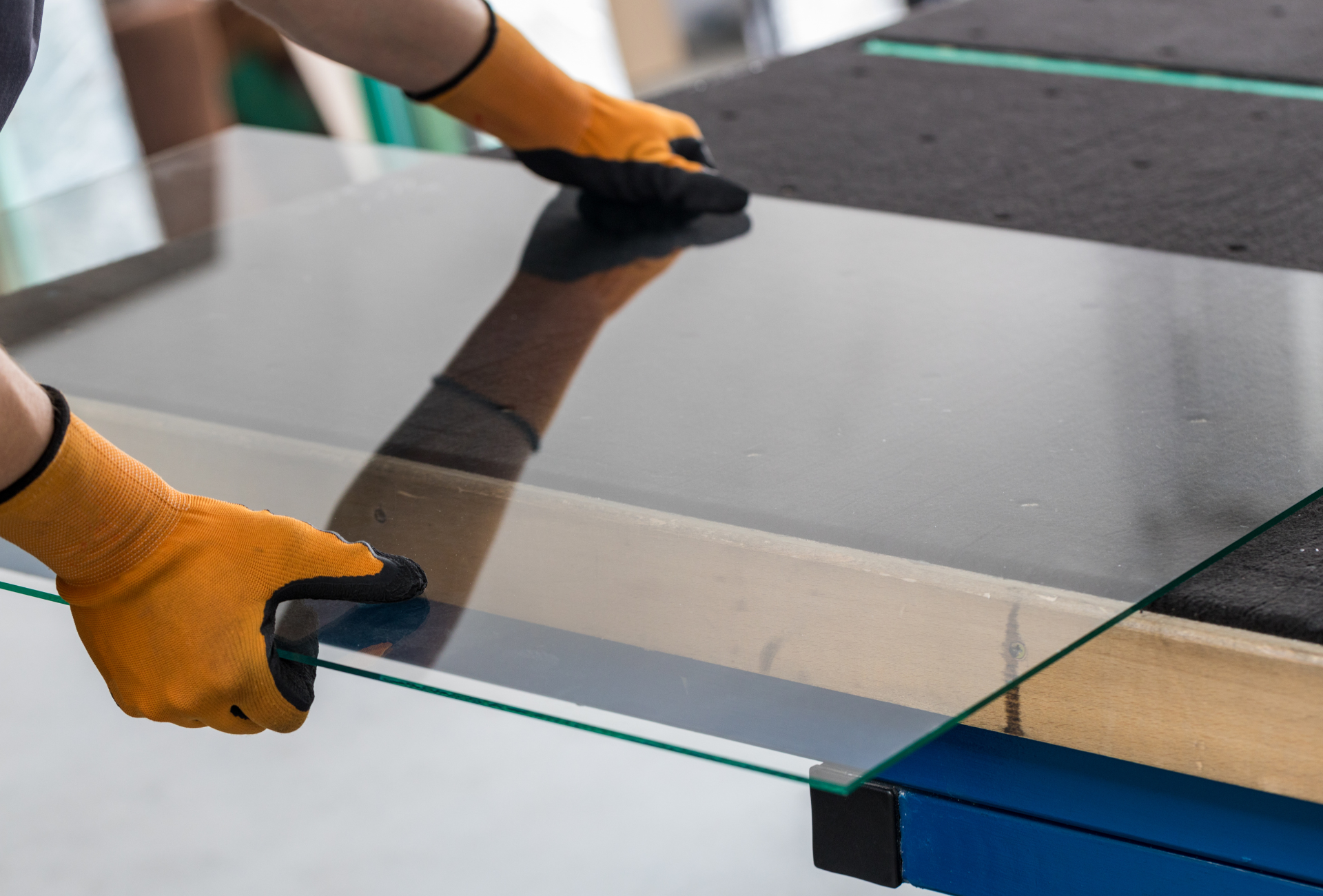 A person wearing orange gloves is cutting a piece of glass