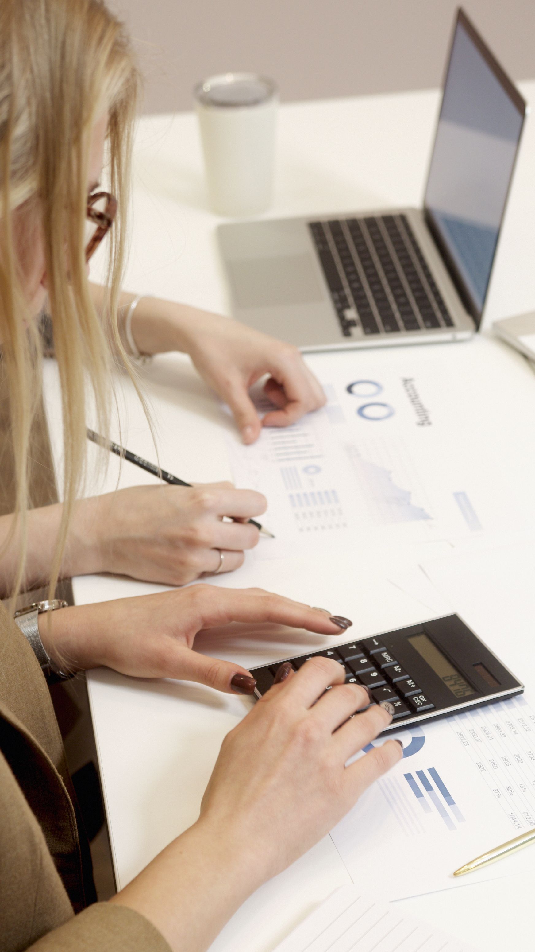 Hand typing on a laptop keyboard beside a calculator on a desk