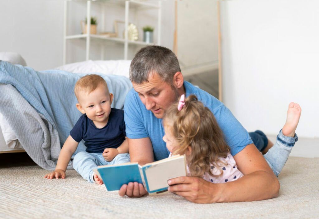 Father reading a book to two young children on a carpeted floor.